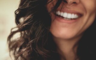 A woman with long wavy black hair smiling with visible white teeth